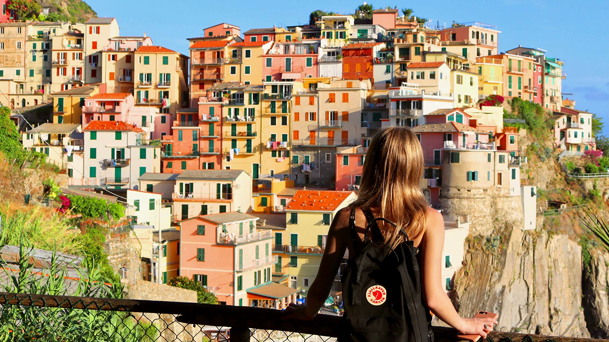 En kvinne med ryggsekk på reise i en fargerik, italiensk by. Foto.