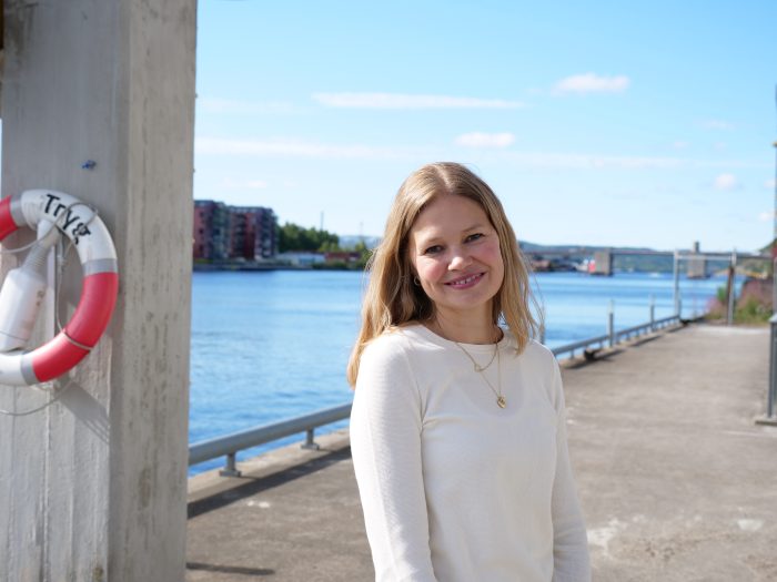 Kvinne med blondt hår og hvit genser ser smilende inn i kamera.