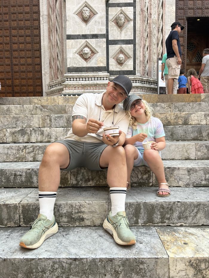 Småbarnsfar og datter sitter på en trapp i Italia og spiser is mens de smiler til kamera
