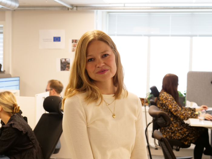 Kvinne står foran et kontorlandskap og ser mot kamera 